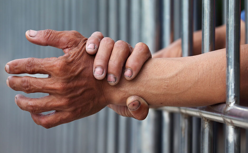 person putting their hands through a jail cell