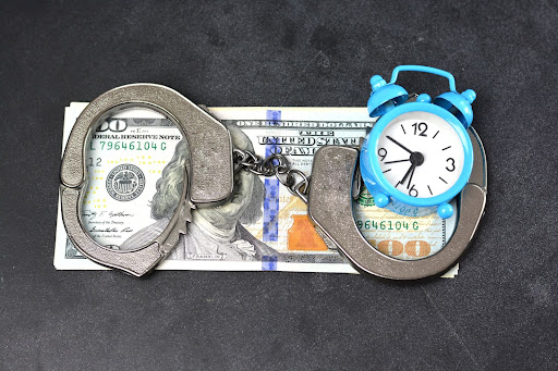One hundred dollar bill with handcuffs and an alarm clock